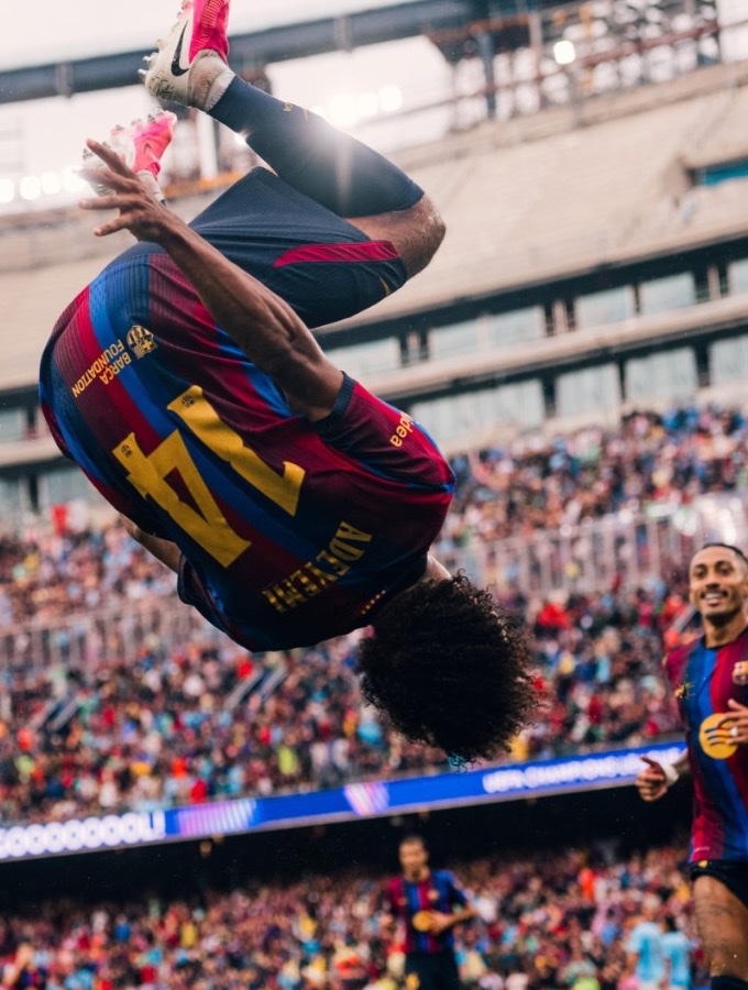 An FC Barcelona player mid-backflip celebrating a goal in a packed stadium